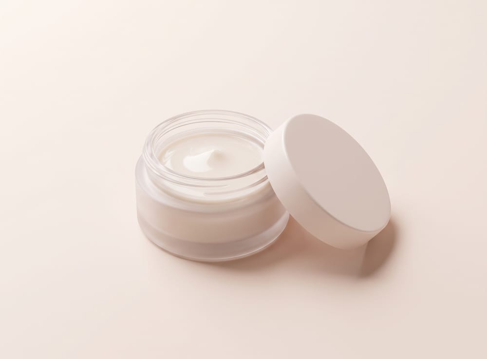 A squat round jar of pale styling gel with the lid off beside it.